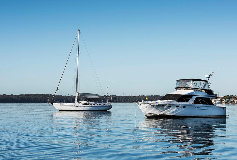 A power boat and sailing boat are moored near each other on calm waters with a blue sky behind.