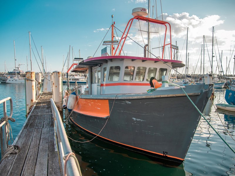 A close up of a fishing trawler. It is wooden, grey and orange. It is moored by a wooden jetty  