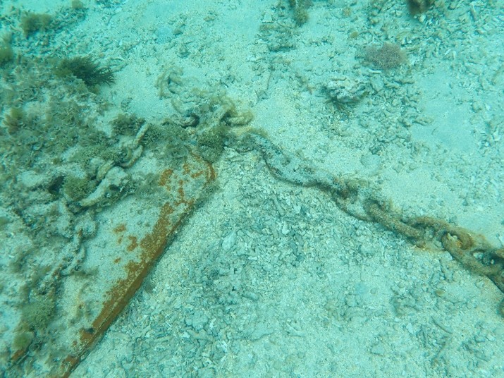 under water we see a metal chain used to moor boats. It is a heavy chain. The chain has scoured the sea bed so that only sand is visible.