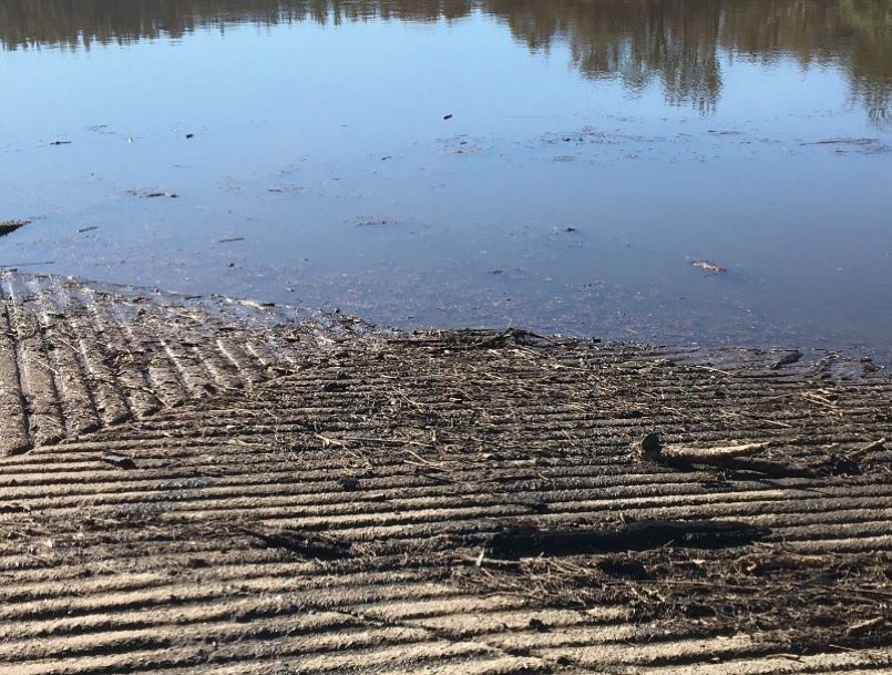 Photo of a boat ramp and the Clyde River after heavy rainfall. There is a lot of ash and sediment on the boatramp and in the water.