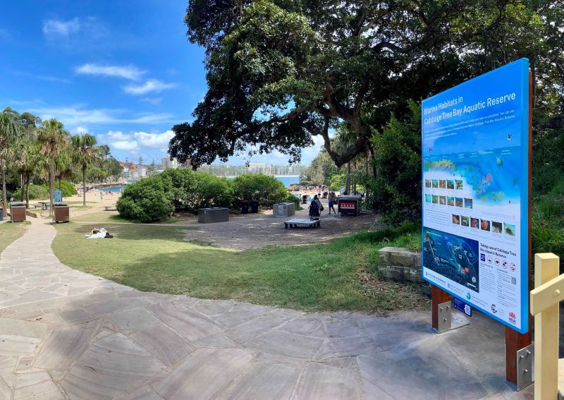 A large detailed sign is placed with Cabbage Tree Bay in the background. 