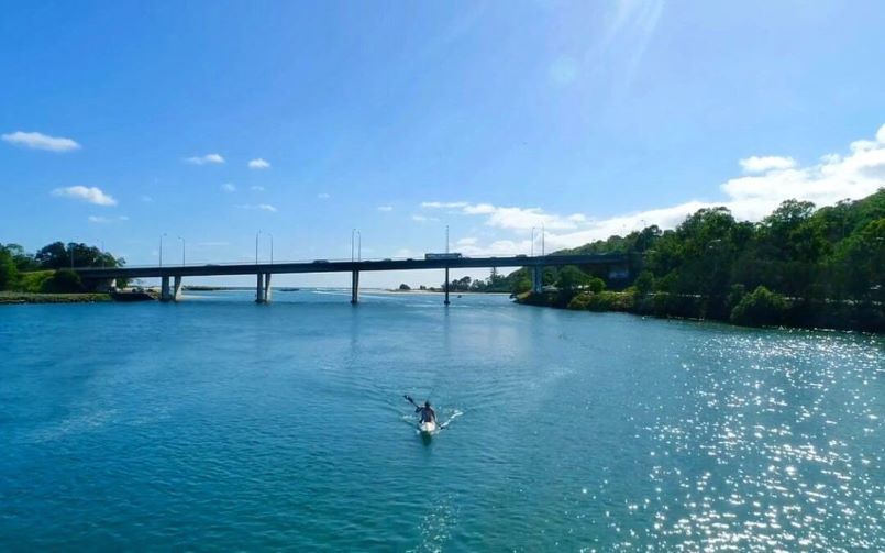 A kayaker paddling on the water in front of a bridge