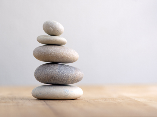 Five smooth stones of different sizes are stacked on top of a timber table.