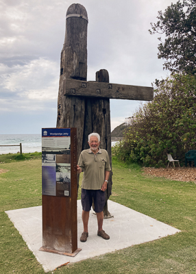A man standing beside an information sign and tall weathered timber.