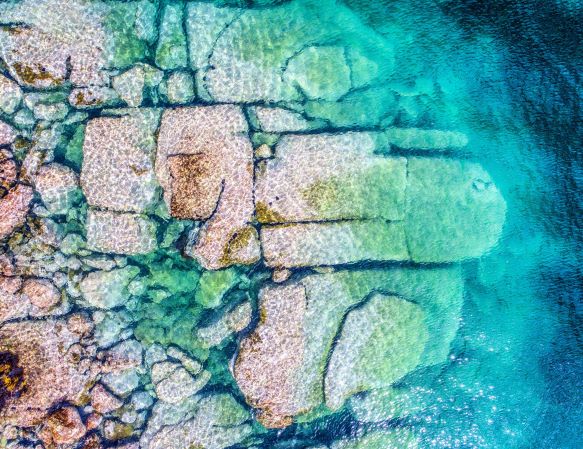 Drone view of aqua water with visible large rock formation.